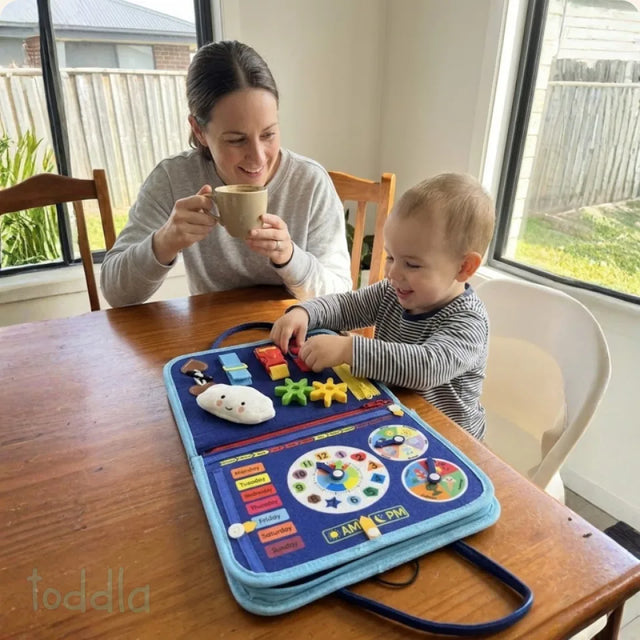 Toddler playing with the Busy Board at the table while a parent eats